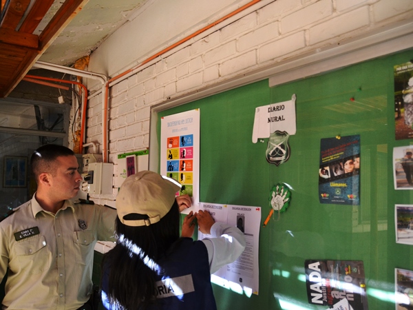 La facilitadora intercultural de la Defensoría, Andrea Mamani, y el cabo de guardia fijan el afiche de derechos en el diario mural del cuartel. 