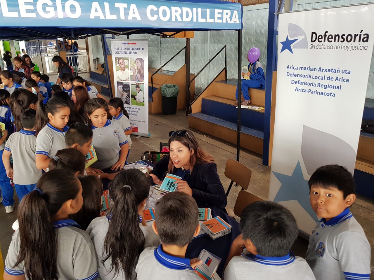 La encargada de comunicaciones de Arica, Daniela Tapia, junto a alumnos del Colegio "Alta Cordillera" que reciben folletería de la DPP.