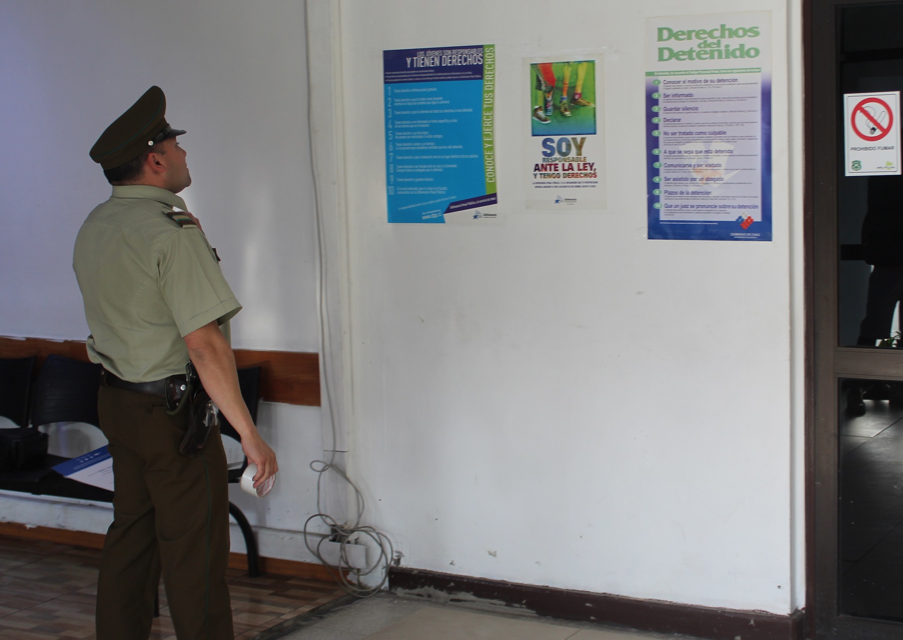 Un carabinero de turno en la Cuarta Comisaría de Santiago observa los afiches sobre los derechos del detenido instalados por la DRMN. 